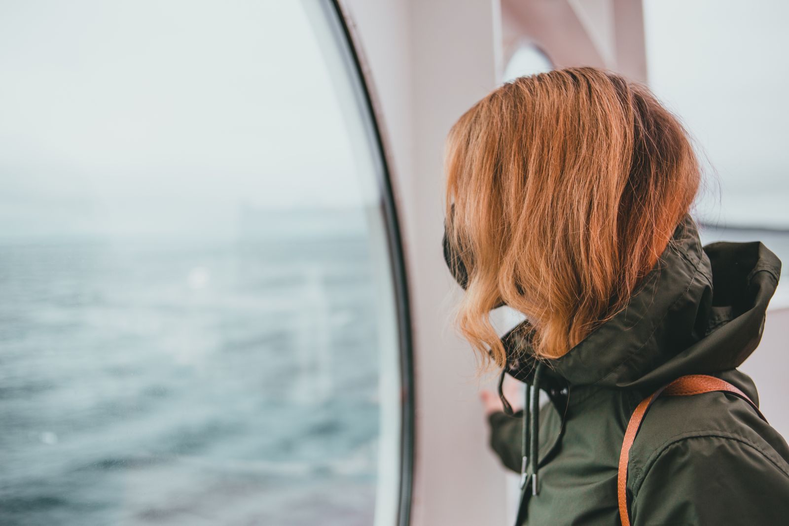 Traveler looking out of a ship window at the sea, phone in pocket, the moment a cruise deals app gets opened