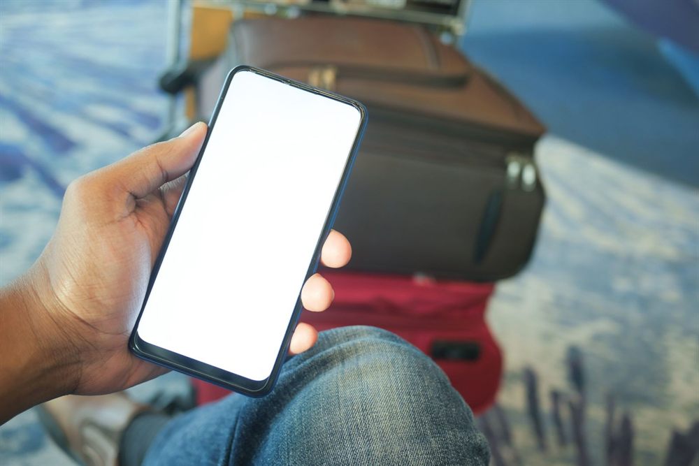 Hand holding a smartphone with luggage in the background