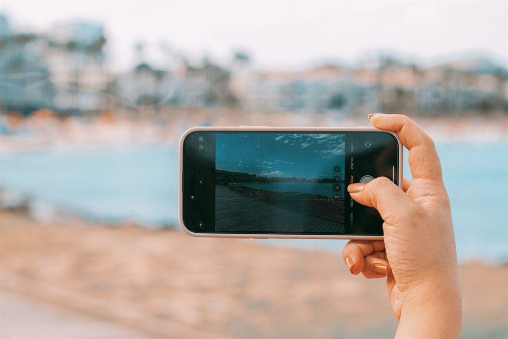 Phone held up to photograph a beach and calm bay