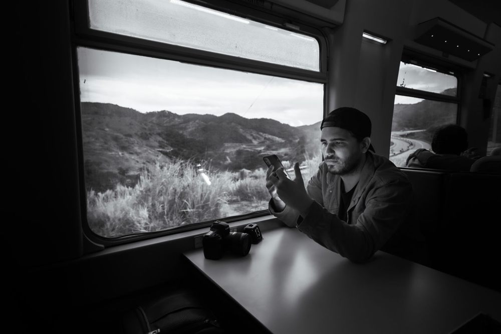 Black and white photo of a traveler using a phone by a train window
