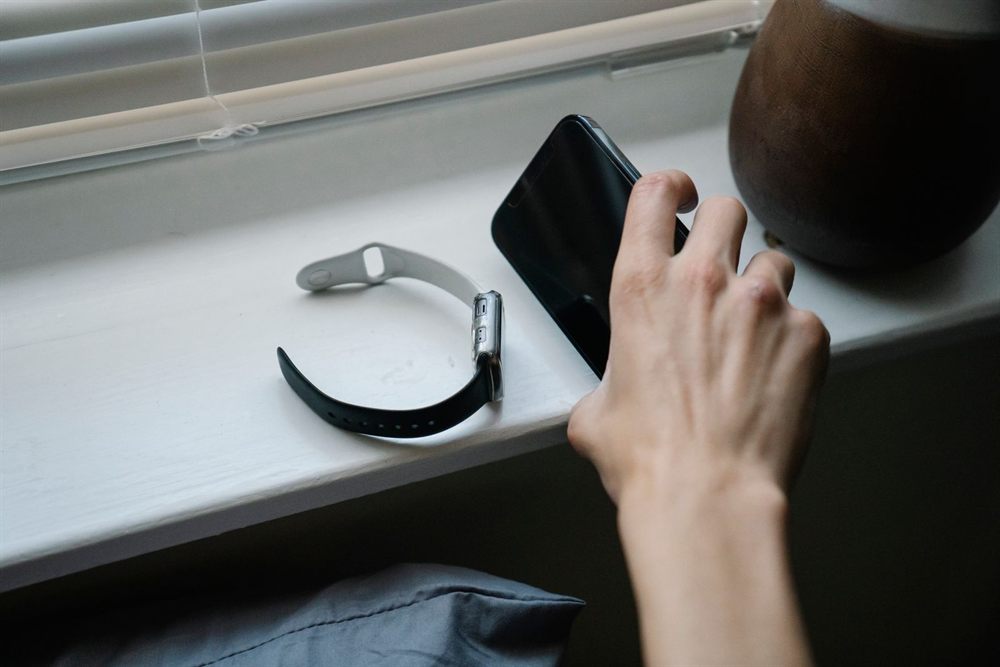 Hand picking up a phone from a windowsill beside a smartwatch