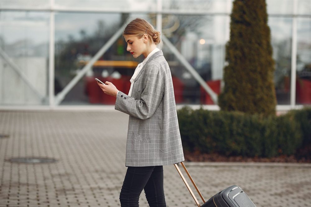 Traveler with a rolling suitcase checking her phone outside a terminal