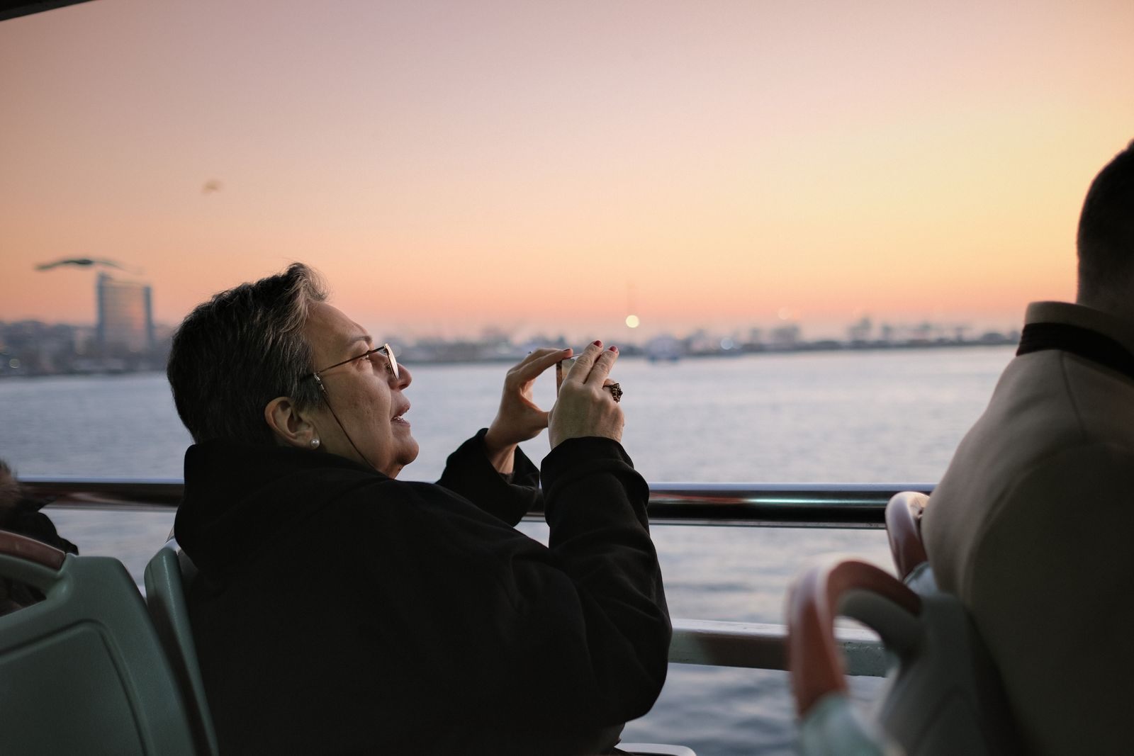 Passenger photographing a harbor sunset with a phone from a ship deck, where cruise price alerts now arrive