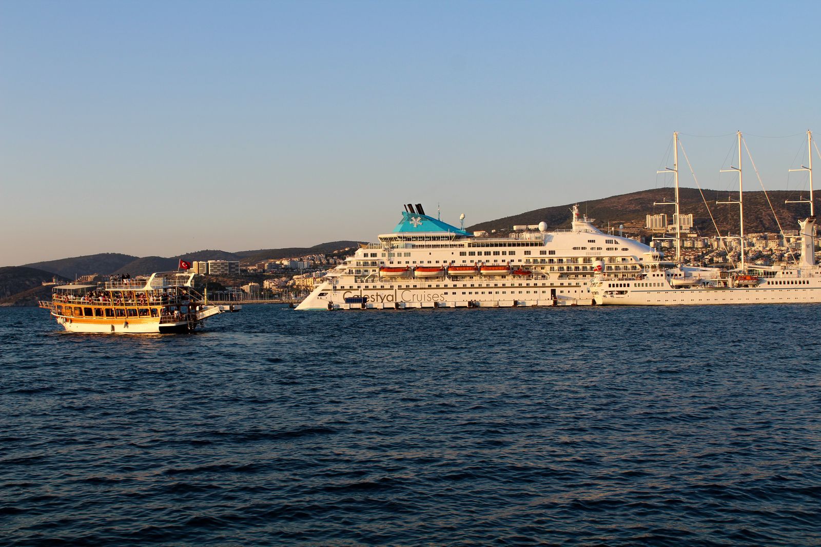 Cruise ship and a tour boat on blue water near a coastal town, where app-only cruise perks come into play